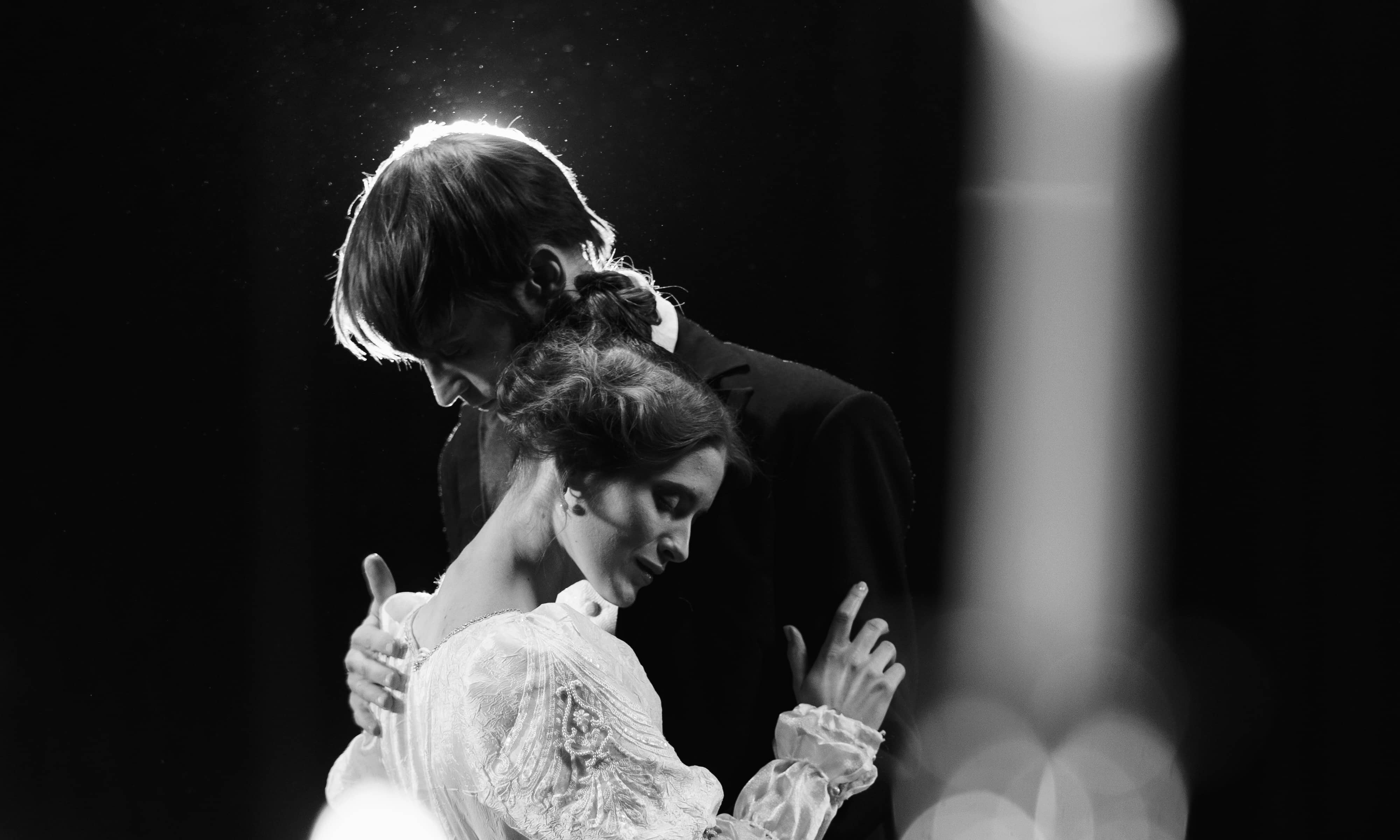 A black and white image of two actors on a stage dancing closly.