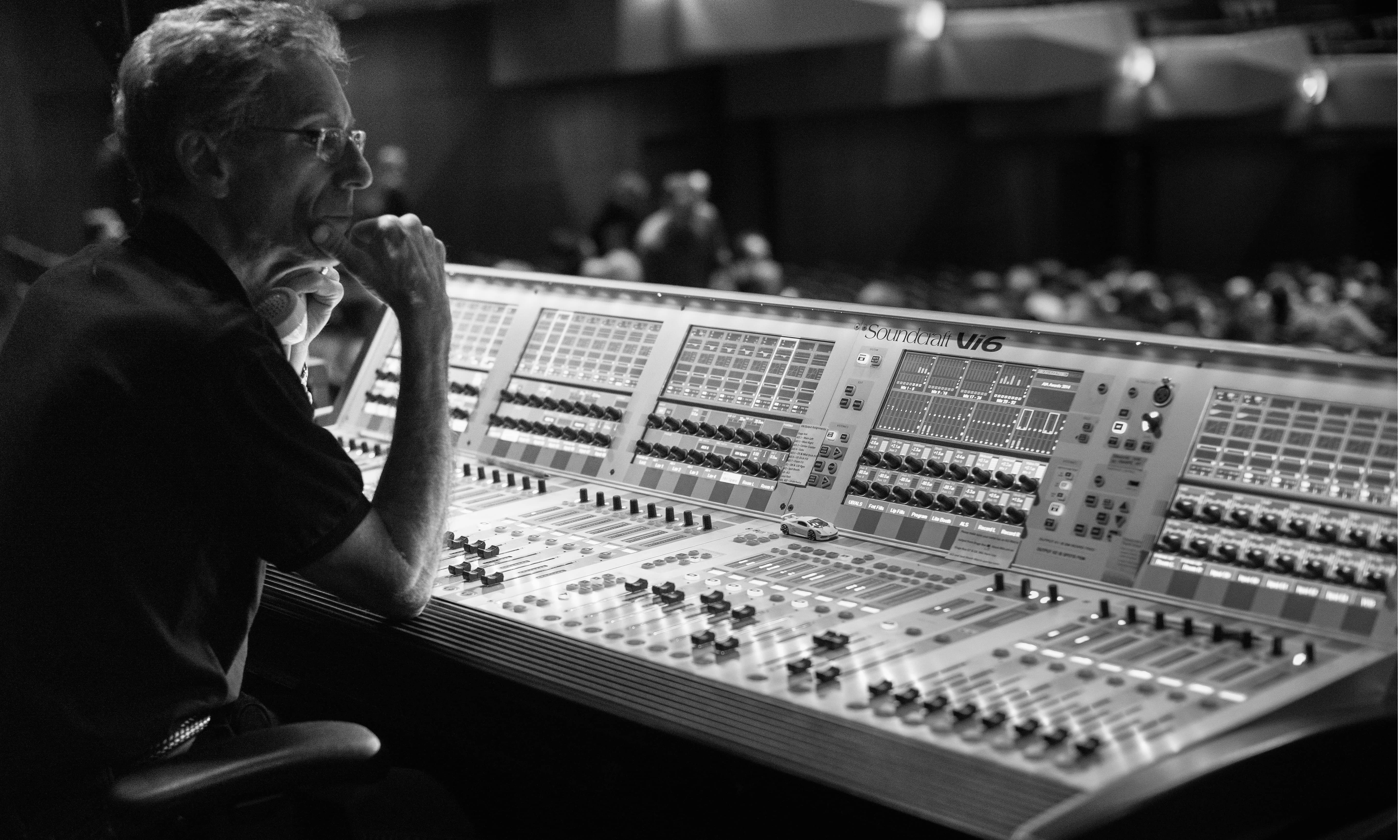 A black and white image of a music producer sitting in front of a board with a lot of buttons to mix music